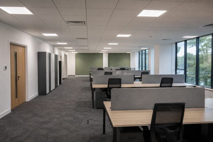 Planta de oficinas terminada: puestos de trabajo con divisiones, sillas de escritorio, luminarias LED empotradas en cielo raso modular y ventanal de piso a techo